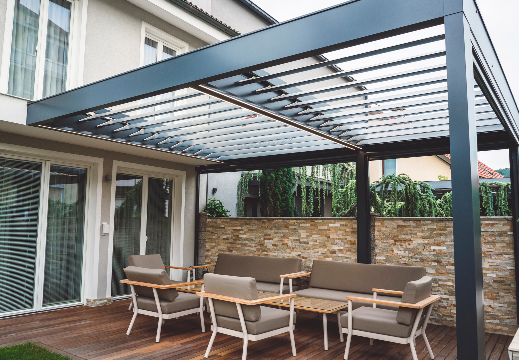 Moderne Lamellenpergola über einer Terrasse mit Lounge-Möbeln an einem Wohnhaus