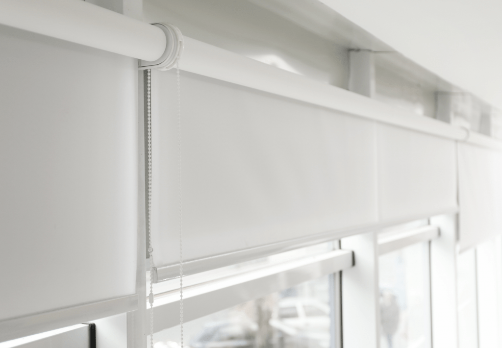 Weiße Innenrollos mit Kettenzug an einer Fensterfront
