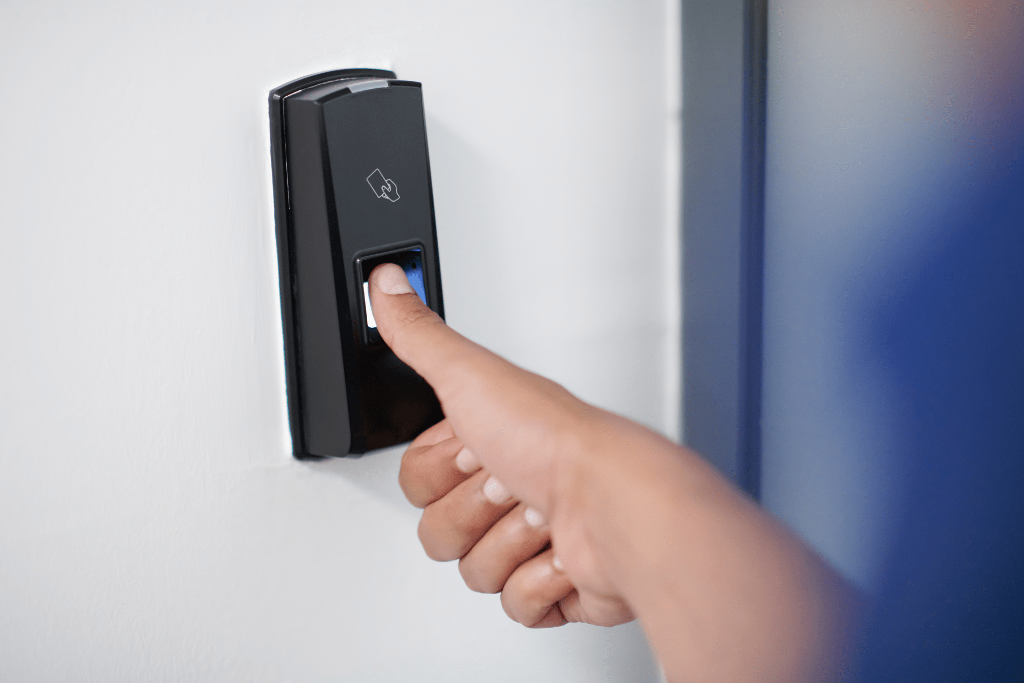 Hand betätigt einen Fingerabdruck-Scanner an einer Wand neben einer blauen Tür