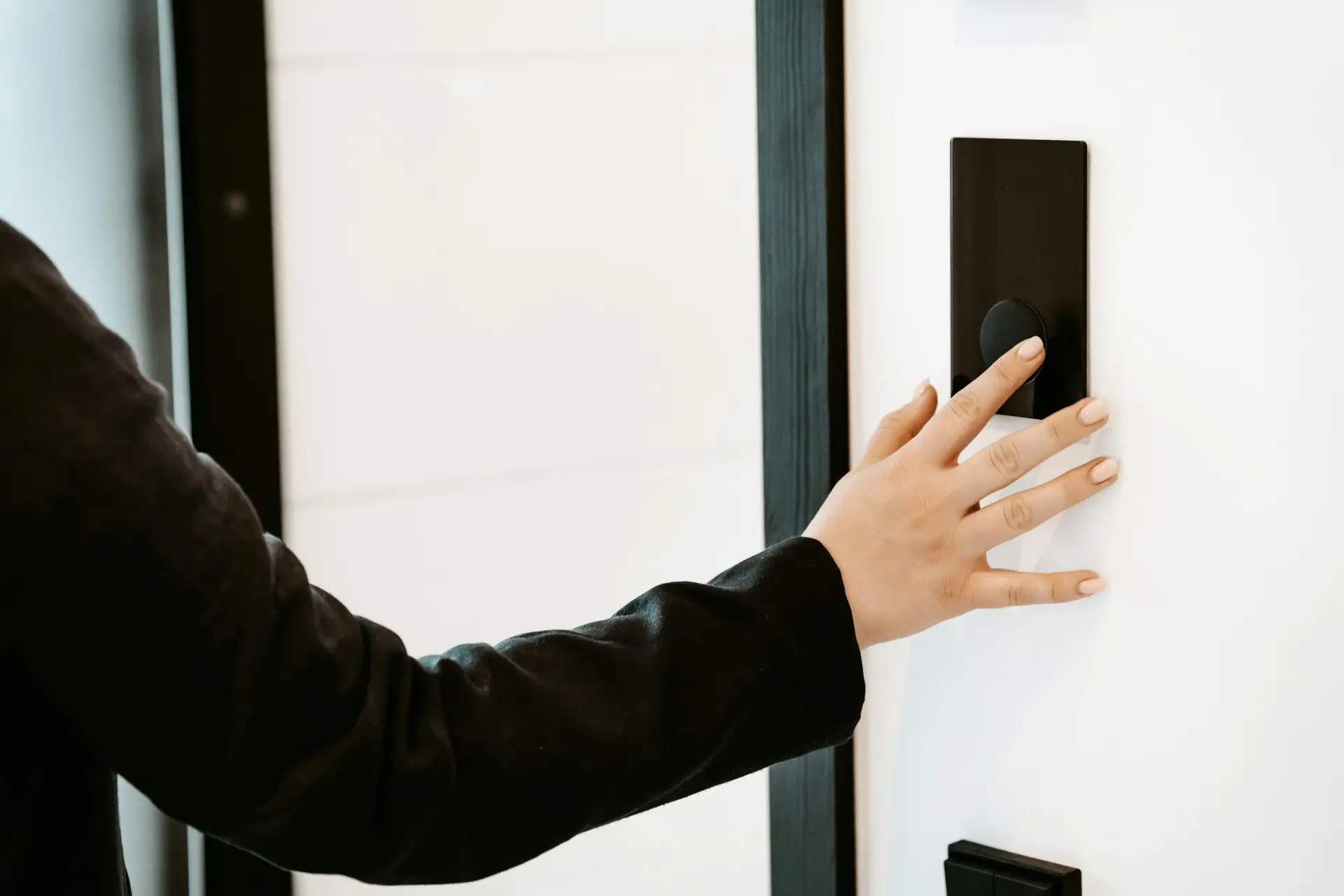 Hand drückt einen schwarzen Türklingel-Knopf an einer weißen Wand